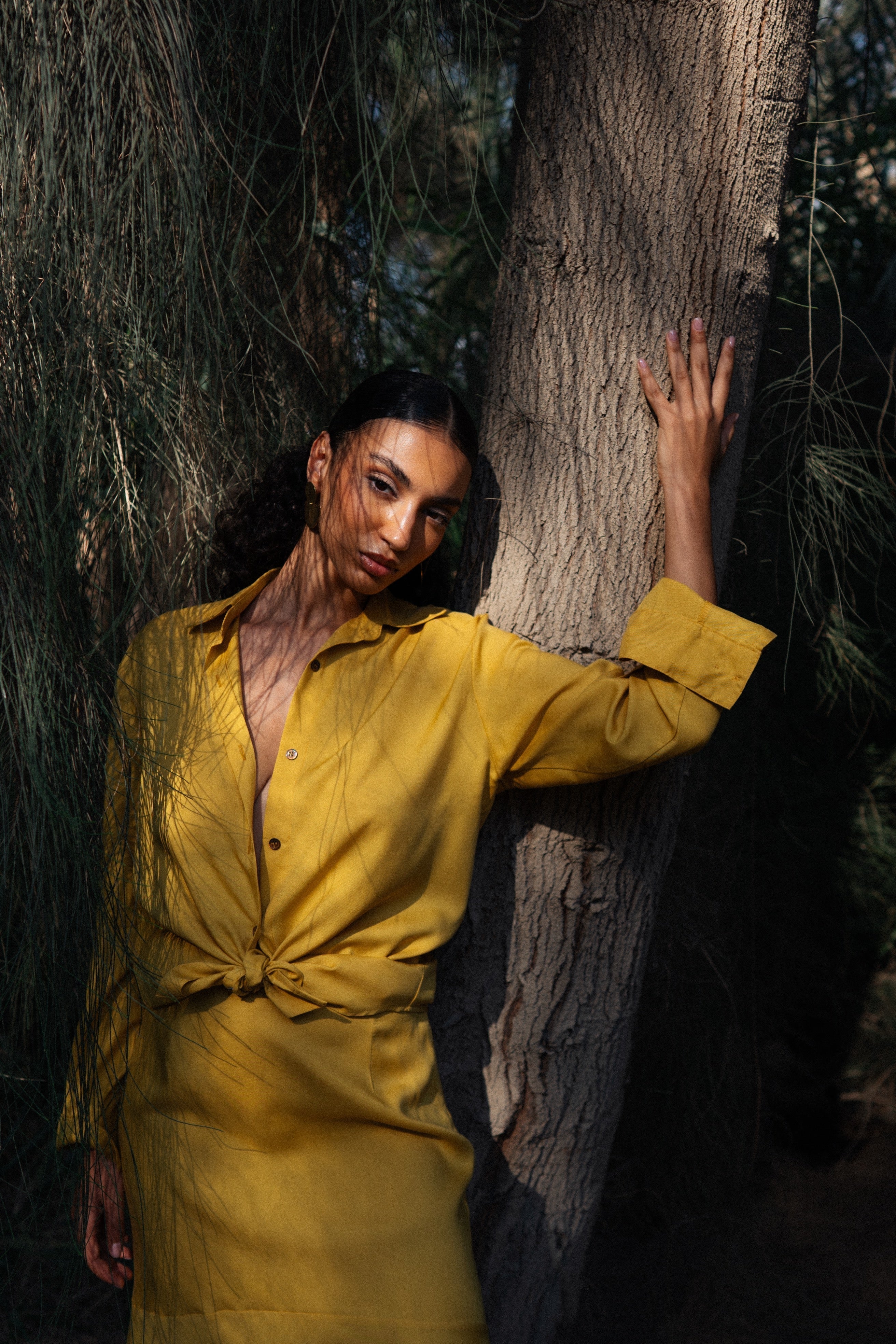 Person in a yellow outfit leaning against a tree in a dark forest setting